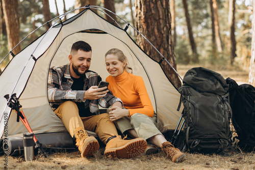 Couple sitting in tent in forest working on laptop