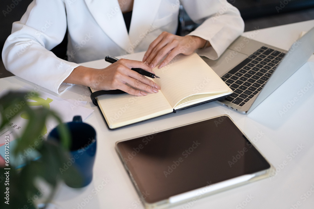 Female entrepreneur using laptop computer and writing planning daily appointment on notebook Female entrepreneur using laptop computer and writing planning daily appointment on notebook