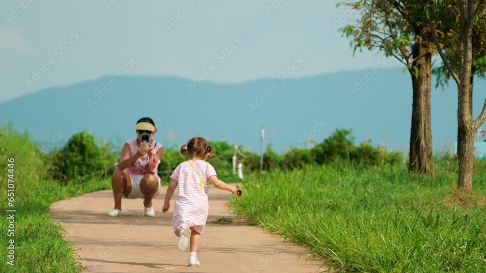 Mom Take Photo of Running Toddler Girl. Multicultural Family in a Park. Korean Mother in Squat Position Recording Phone Video of Little Daughter Running Towards Her on Walkway in Mountain Landscape Mom Take Photo of Running Toddler Girl. Multicultural Family in a Park. Korean Mother in Squat Position Recording Phone Video of Little Daughter Running Towards Her on Walkway in Mountain Landscape