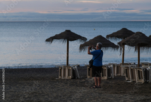 Canvastavla señor mayor haciendo fotos al amanecer en la playa