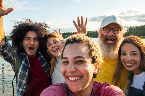 Multiracial young group of trendy people having fun together on vacation - Diverse millennial friends taking selfie portrait together while enjoying free time on a forest lake beach - Friendship #651085454