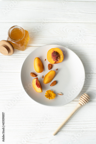 A plate with an apricot, honey and a honey spoon on a white background