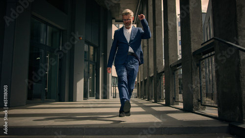 Funny moving happy Caucasian senior business worker employee mature man businessman dancing walking on stairs near office building outdoors walk dance celebrate achievement having fun fooling around © Yuliia