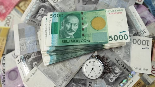 Stack 1000 and 5000 Kyrgyz som denomination bills and old pocket watch slowly rotating surface, Kyrgyz Republic national paper currency, close-up. Financial success and abundance. Loan debt reminder. photo