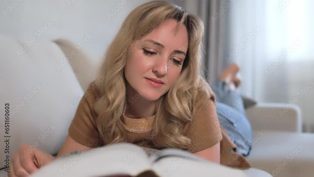 A blonde woman with curls on the sofa reads a book. A blonde woman with curls on the sofa reads a book.