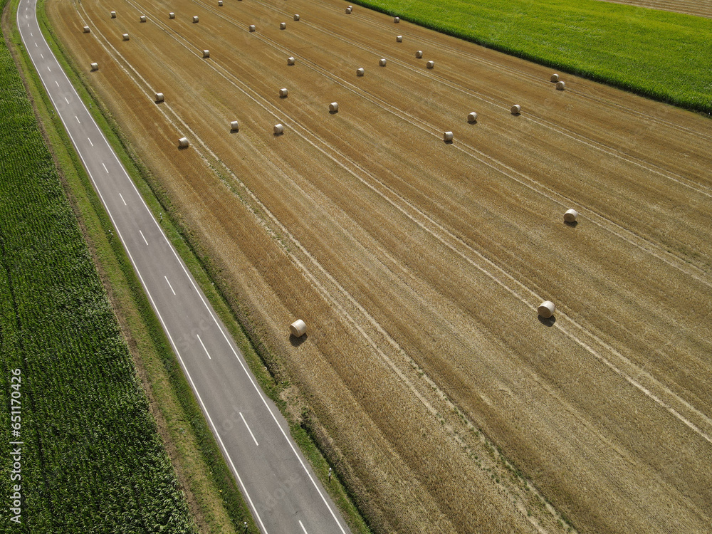 Fototapeta premium Aerial view of a landscape with a road between a cornfield and a grass field with hay bales