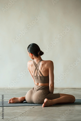 Flexible body, sitting, rear view. Young woman with slim body type is in fitness clothes in the studio