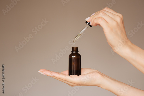 human's hand holds a dark bottle of cosmetic liquid and drips into it with a pipette. isolated on a light background