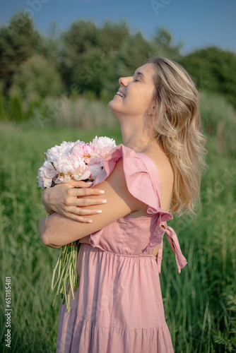 Portrait ofyoung charming woman with loose hair in pink dress with bouquet of peonies in nature. photo