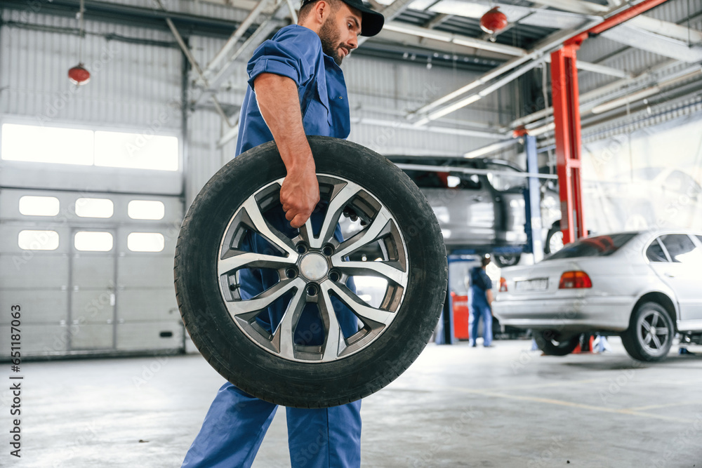 With brand new wheel. Auto mechanic working in garage. Repair service With brand new wheel. Auto mechanic working in garage. Repair service