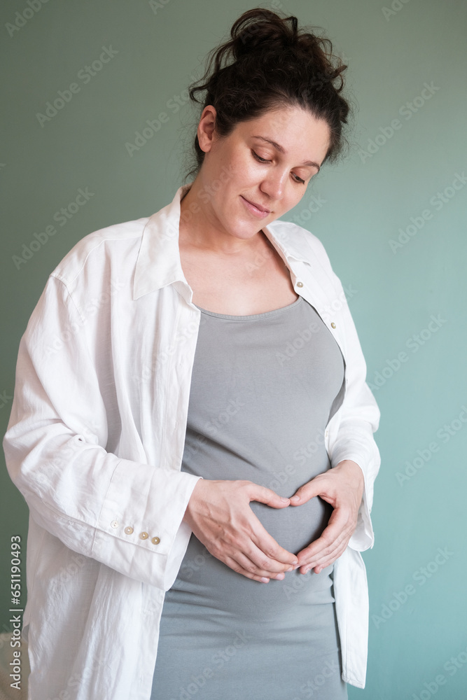 Vertical photo of the expectant mother. A pregnant woman with a big belly in her third trimester folded her hands in a heart shape on her tummy. Expecting a baby and happy parents. Vertical photo of the expectant mother. A pregnant woman with a big belly in her third trimester folded her hands in a heart shape on her tummy. Expecting a baby and happy parents.