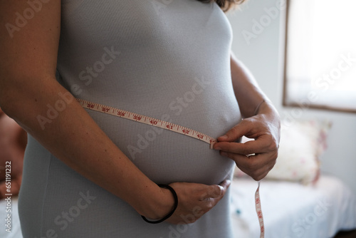 Health of a pregnant woman. Close-up of a big belly of a young pregnant woman who measures her abdominal volume with an inch tape. Weight control during pregnancy and gynecology.
