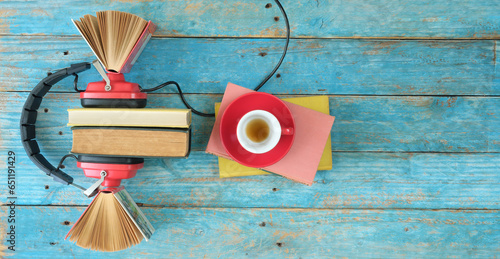 audio book concept with row of books cup of coffee and vintage red headphones,flat lay on blue wooden planks, free copy space