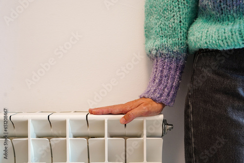 woman in winter sweater next to a central heating in the home. increase the electricity price for warming in winter season