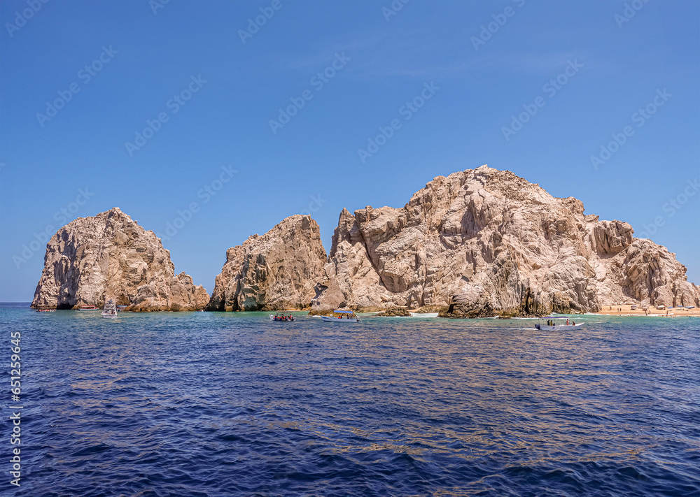 Mexico, Cabo San Lucas - July 16, 2023: Reserva de Lobos Marinos landsend between ocean and Playa de los Amantes, lovers beach under blue sky. Small sightseeing boats in front Mexico, Cabo San Lucas - July 16, 2023: Reserva de Lobos Marinos landsend between ocean and Playa de los Amantes, lovers beach under blue sky. Small sightseeing boats in front