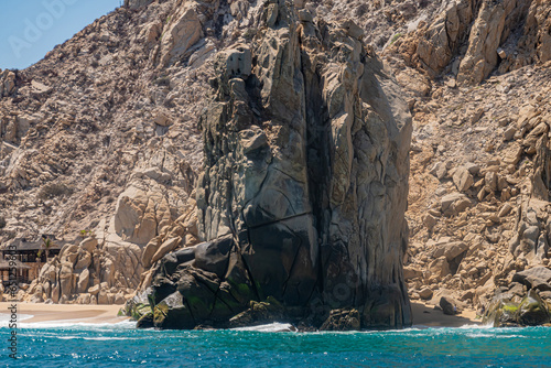 Mexico, Cabo San Lucas - July 16, 2023: Brown-beige Rock blocks west end of Playa de los Amantes. More west: Grand Solmar Resort with private beach starts. Greenish ocean water in front. photo