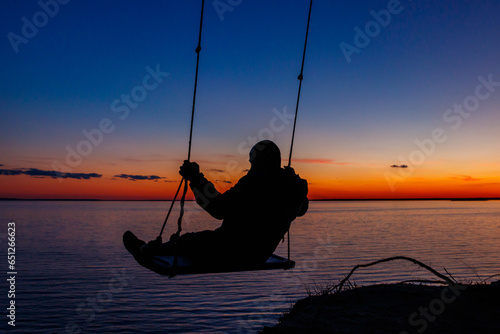 Silhouette of a man on rope swing above river at sunset