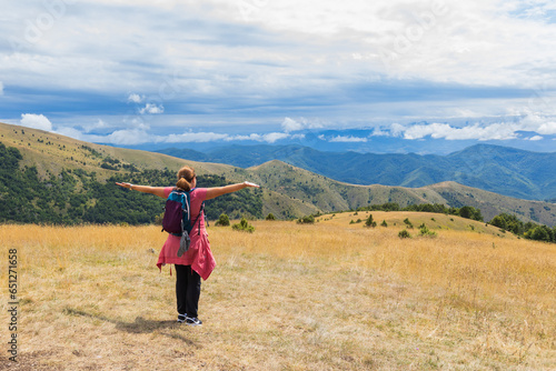 Happy woman with outstretched arms relaxing on mountains peak, stunning summer nature landscape.