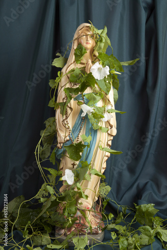 a statuette of the Virgin Mary covered with bindweed in front of a wavy green curtain