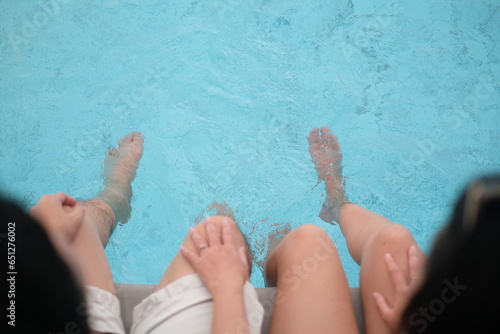 Relaxing moment of two people dipping their feet into a clear swimming pool.