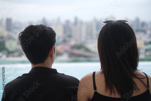 Back view of a couple relaxing together while admiring a modern city skyline.
