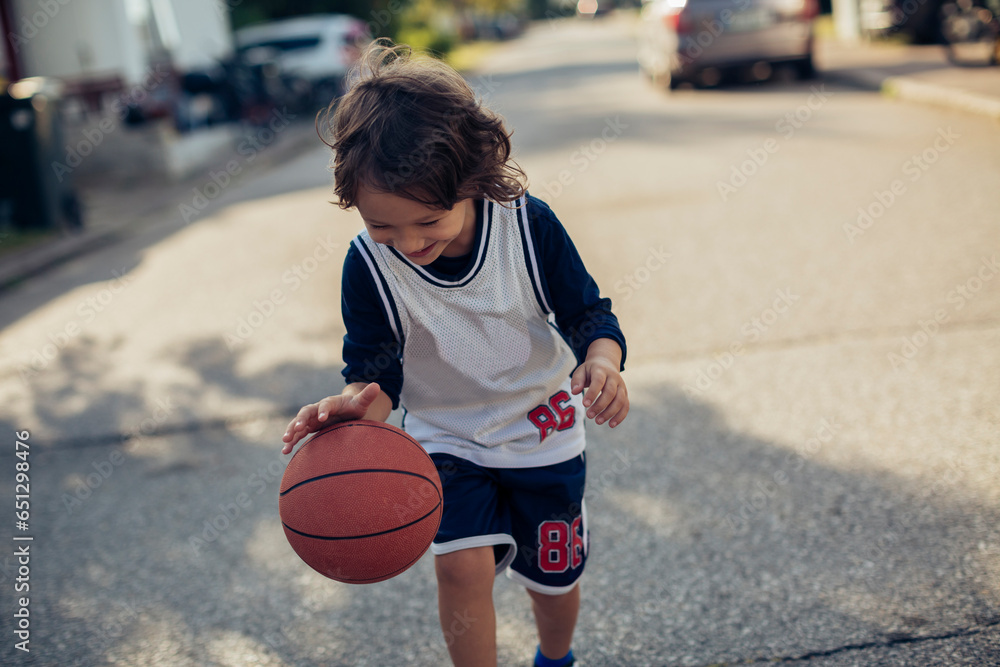 Happy young boy having fun and playing with a basketball in the street of a suburb Happy young boy having fun and playing with a basketball in the street of a suburb
