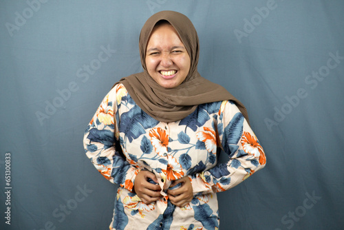 muslim woman with stomach ache, menstrual period cramp, abdominal pain, food poisoning hands gesture. isolated over grey background. asian woman photo concept