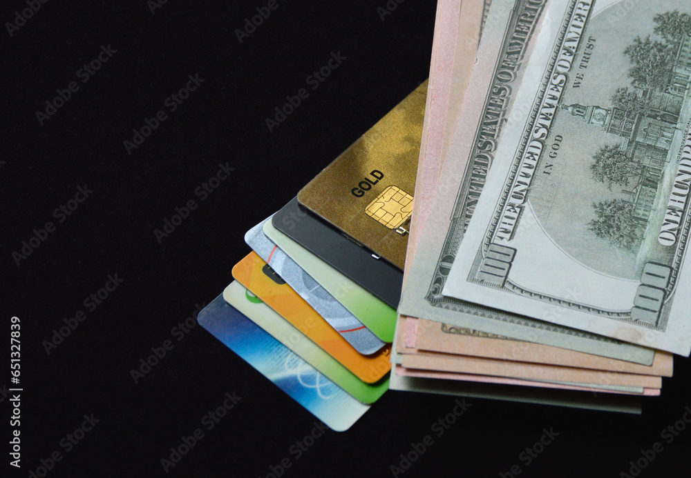 bank plastic credit cards and debit cards and us dollars on a black background. transition from paper money to non-cash and electronic payments and purchases. refusal of paper pulp bank plastic credit cards and debit cards and us dollars on a black background. transition from paper money to non-cash and electronic payments and purchases. refusal of paper pulp