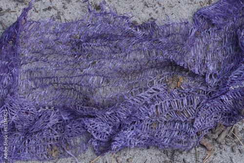 a piece of old crumpled purple plastic mesh lies on the gray sand on the street