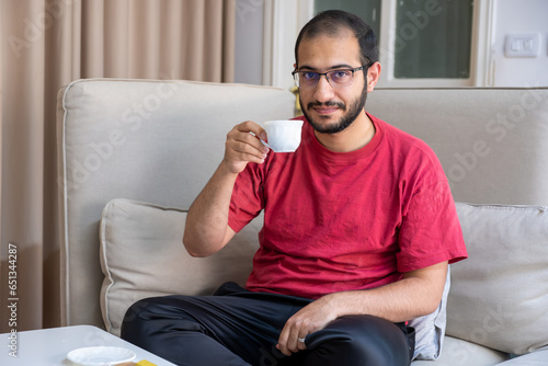 Young bearded male drnking coffee and smiling  in living room photo