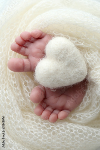 Knitted white heart in the legs of a baby. The tiny foot of a newborn baby. 