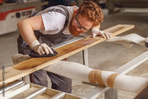 Obraz na plátně Professional carpenter coating a wooden board with protective oil in a workshop