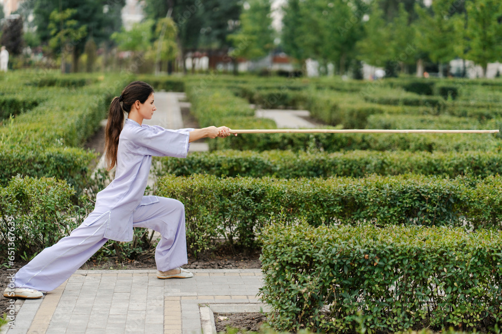 Young lady fighter with stick in hands wearing kimono training at the summer park alone