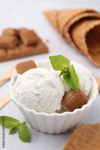 Scoops of tasty ice cream with mint leaves and caramel candies on white table, closeup
