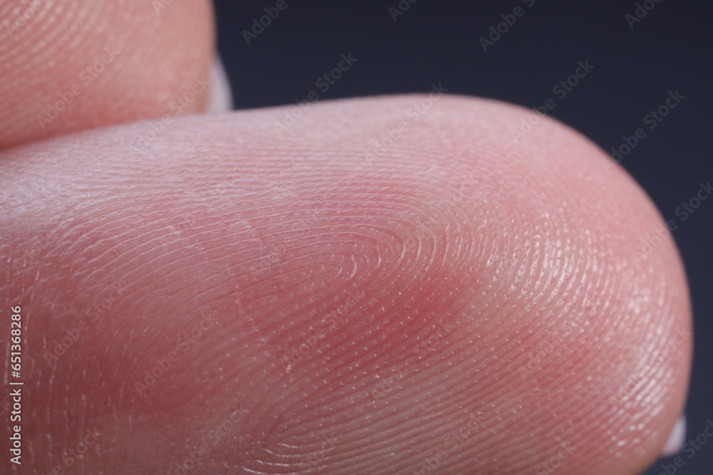 Finger with friction ridges on dark background, macro view Finger with friction ridges on dark background, macro view