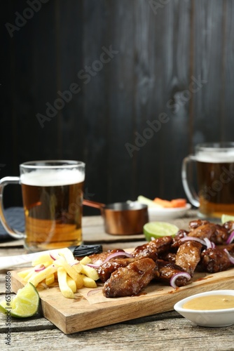 Tasty roasted chicken wings served with beer on wooden table. Space for text