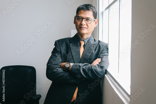 Portrait of successful Asian mature businessman standing confidently at the office