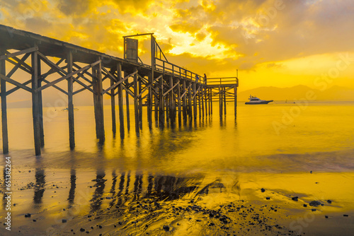 A wooden pier juts out into a calm body of water, bathed in the golden light of sunrise. photo