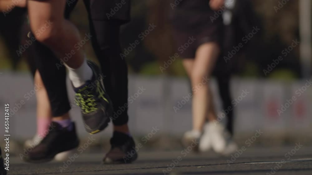 Close-up view from the ground, from the side a crowd of running people in sports clothes on the asphalt on a sunny day. People participate in a race, a marathon around the city Close-up view from the ground, from the side a crowd of running people in sports clothes on the asphalt on a sunny day. People participate in a race, a marathon around the city