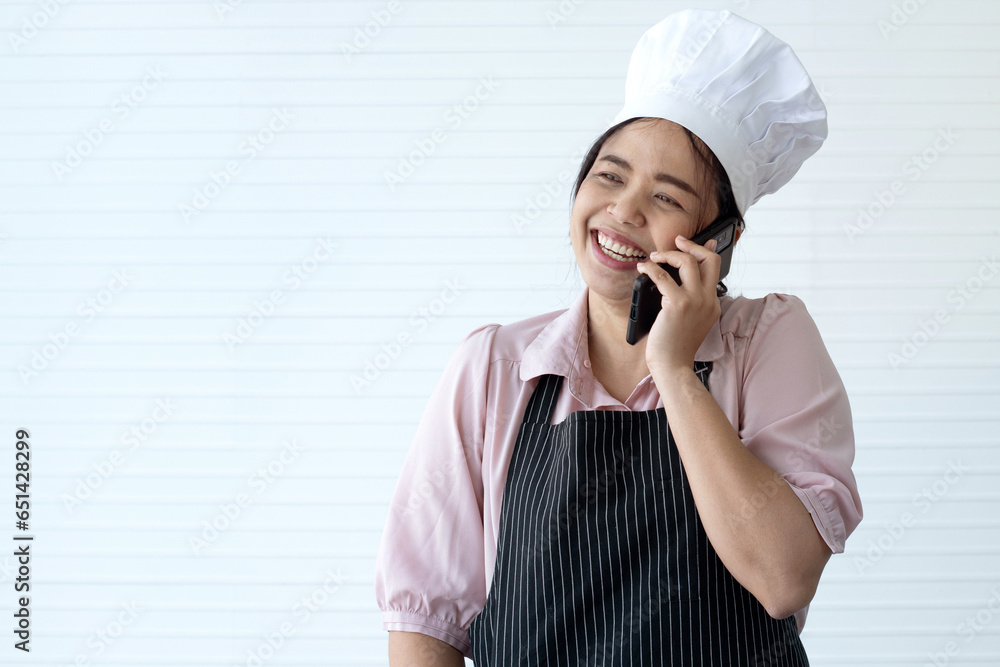 Happy female chef in black apron and chef hat on white background, smiling and talking on smartphone Happy female chef in black apron and chef hat on white background, smiling and talking on smartphone