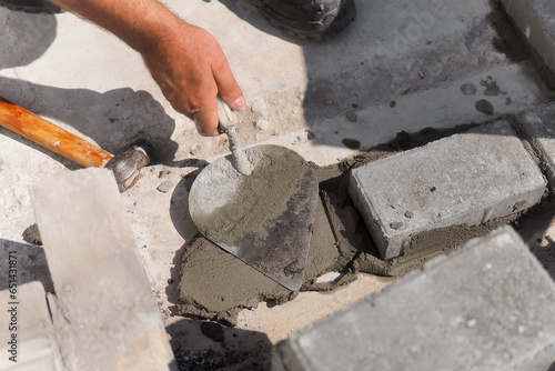 Mason lays out brickwork from gray bricks. Hands of builder with trowel close-up. Man works at construction site. Background.