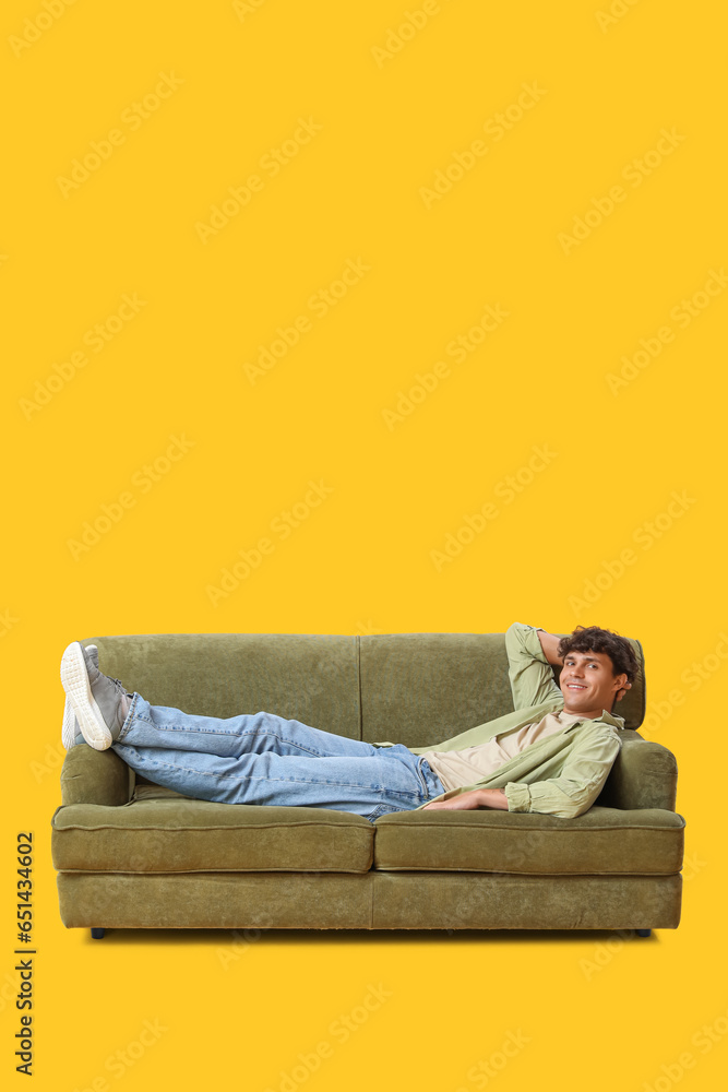 Young man resting on sofa against yellow background