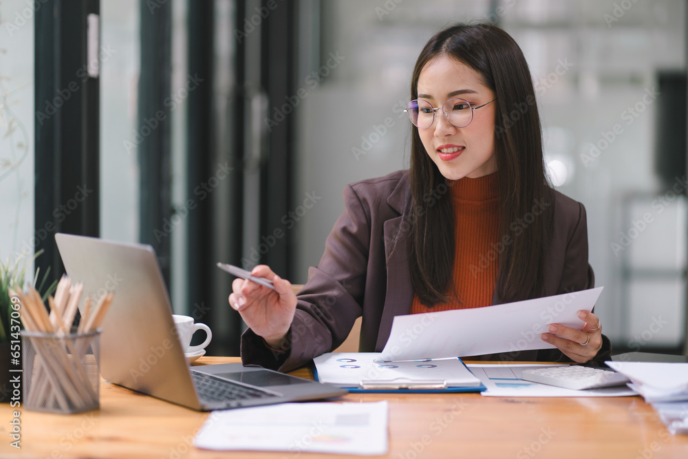 Asian businesswoman or accountant using a calculator, graphs, and charts to analyze market data, balance sheets, accounts, and net profits. Asian businesswoman or accountant using a calculator, graphs, and charts to analyze market data, balance sheets, accounts, and net profits.