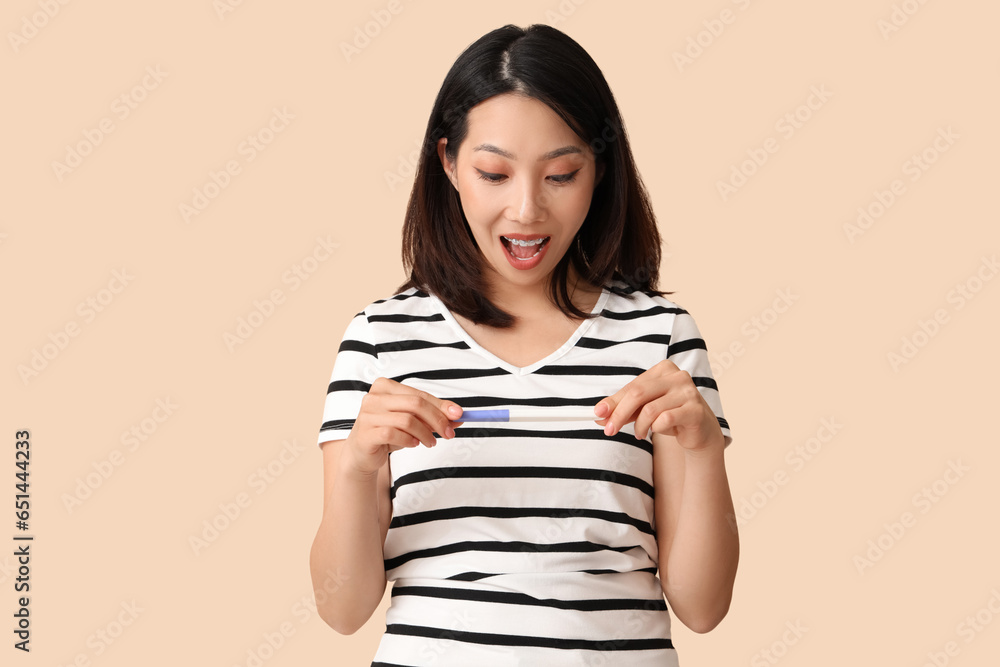 Happy beautiful young Asian woman with pregnancy test on beige background Happy beautiful young Asian woman with pregnancy test on beige background