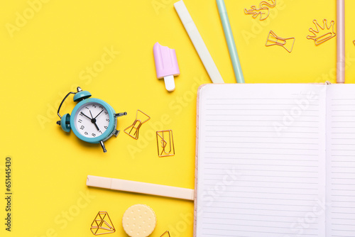 Notebook with different stationery supplies on yellow background