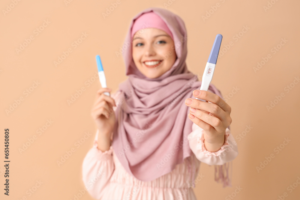 Happy Muslim young woman with positive pregnancy tests on beige background Happy Muslim young woman with positive pregnancy tests on beige background