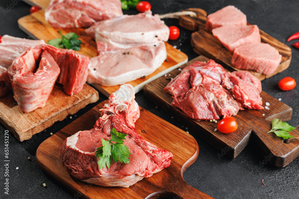 Variety of raw beef meat and pork ribs, pig steaks for grilling with seasoning on wooden board, dark rustic background
