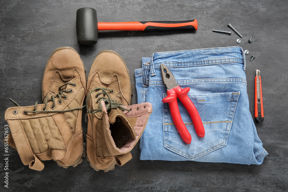 Pair of work boots, jeans and different tools on black grunge background. Labor Day celebration