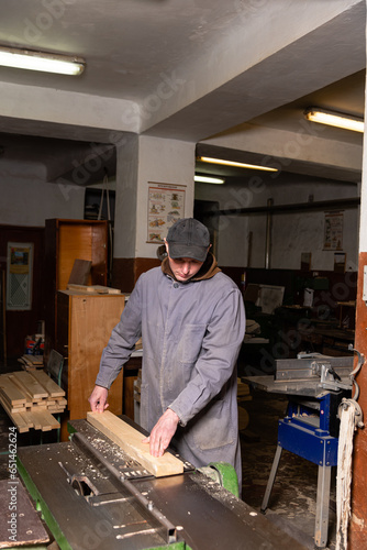 A craftsman works on woodworking machines and saws in a furniture workshop