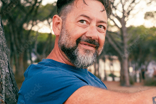 Side closeup portrait of adult man with beard smiling and enjoying relax time at the park. Happy and serene people with cheerful expression. Good day. Handsome male 50 years old outside. Nature place